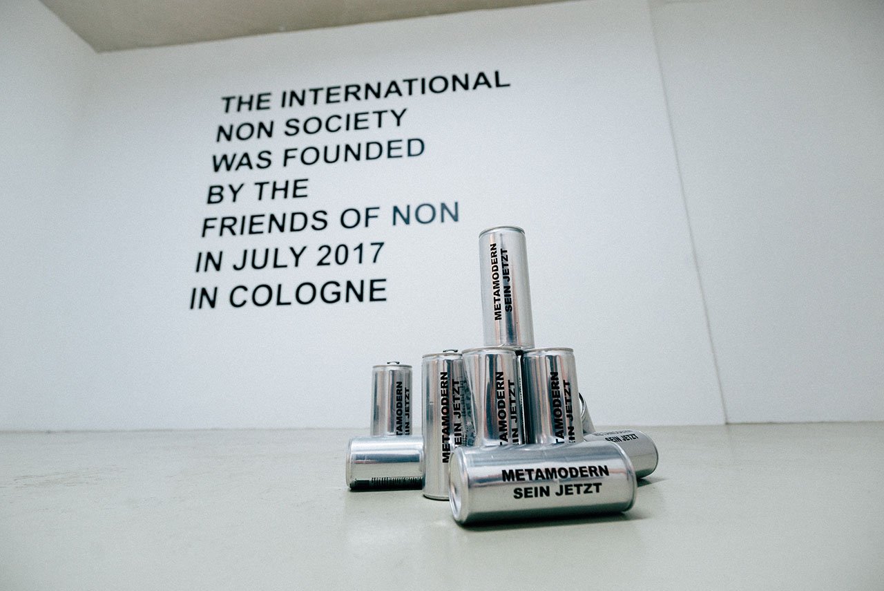 Wall text THE INTERNATIONAL NON SOCIETY and stacked aluminium cans METAMODERN SEIN JETZT